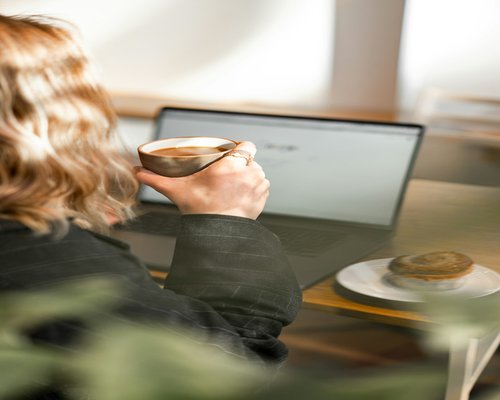 Close up of hands typing on a laptop with a cup of Colombian coffee nearby