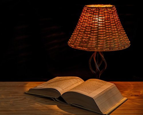 A warm desk lamp illuminating an open book in a dimly lit room